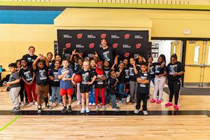 A group of children smiling and posing together for a photo in a gym setting with University of Wisconsin Badger basketball star Carter Gilmore and Exact Sciences staff 