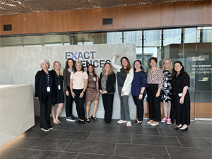 Exact Sciences team members and Patient Advocacy Advisory Council members pose for a group photo in front of the Exact Sciences logo. 